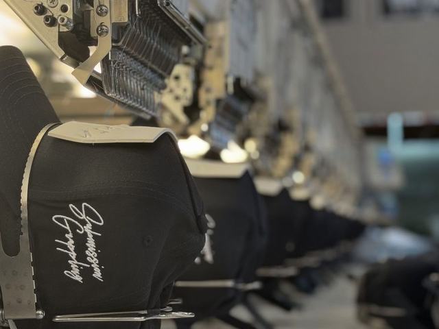 Multi-head embroidery machine stitching logos onto a run of black caps