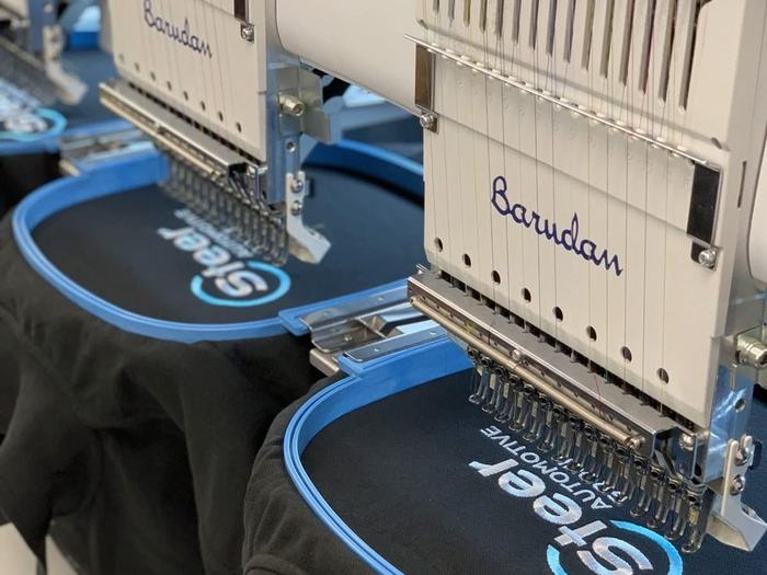 Barudan embroidery machines stitching a company logo onto black polo shirts