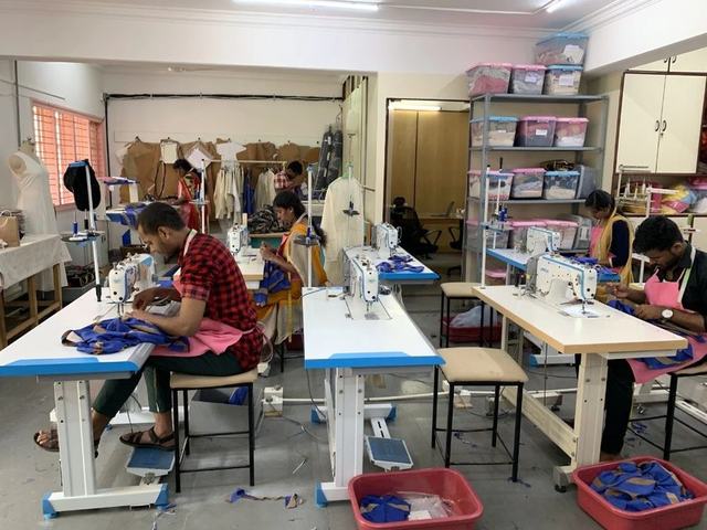 Tailors stitching uniforms on the production floor at Knit Wear Capital